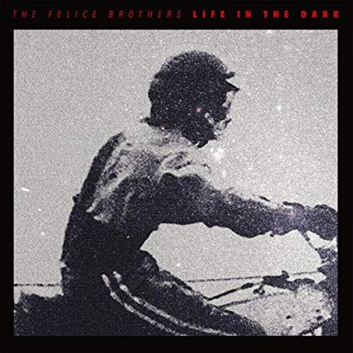 Black and white grainy image of a person with a cap, playing drums.