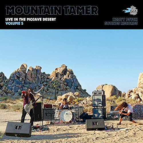 Band performing outdoors amidst rocky desert landscape, vinyl record cover.
