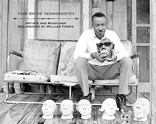 Black and white photo of a man with sculpted heads on a porch.