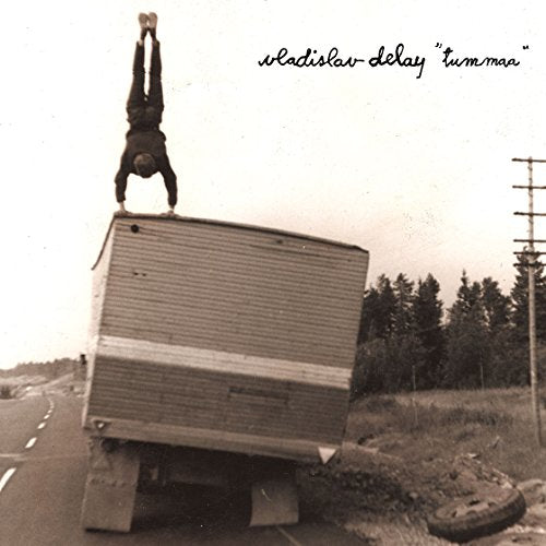 "Sepia-toned album cover: man doing handstand on overturned truck by a road."