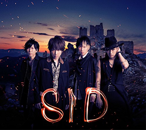 Four men in dark clothing stand before a castle at sunset.