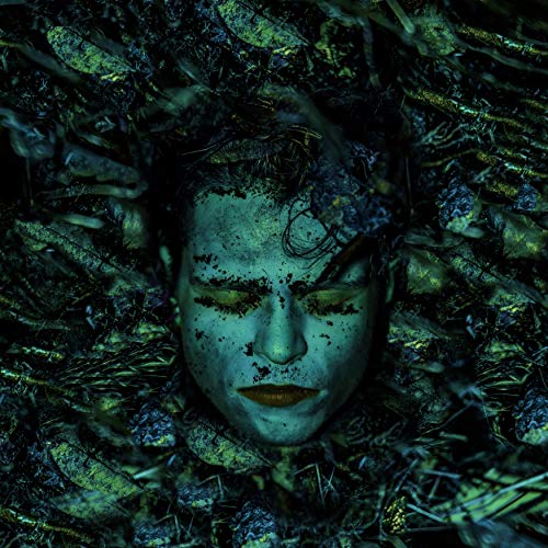 Pale face with closed eyes, surrounded by dark, textured foliage.
