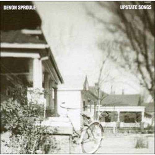 "Album cover featuring a black and white photo of a bicycle outside a house."