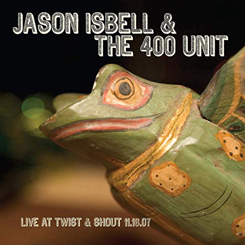 A vinyl record cover featuring a green, wooden frog statue against a dark background.