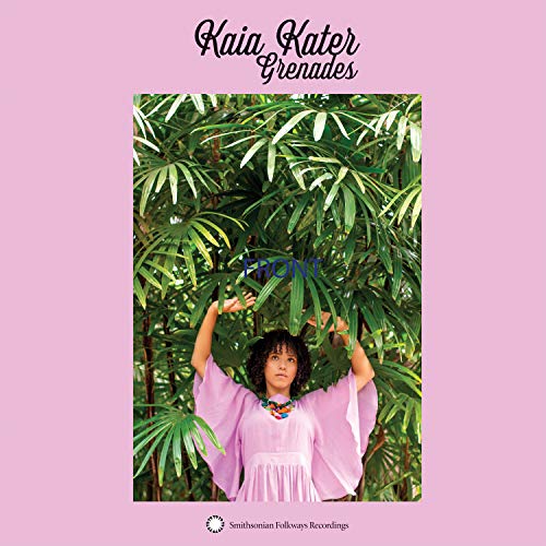 A woman in a pink dress stands among green leaves with raised arms.