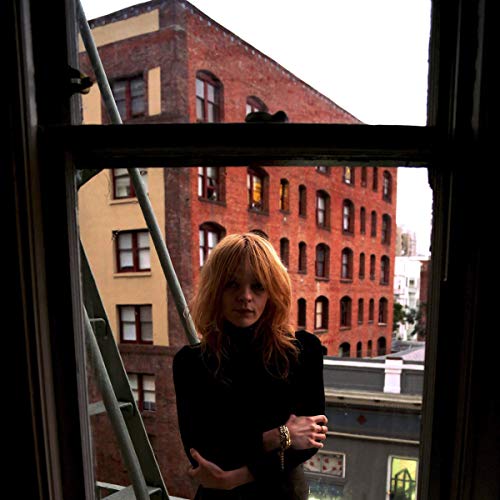 A woman with reddish hair stands in a window overlooking a brick building.