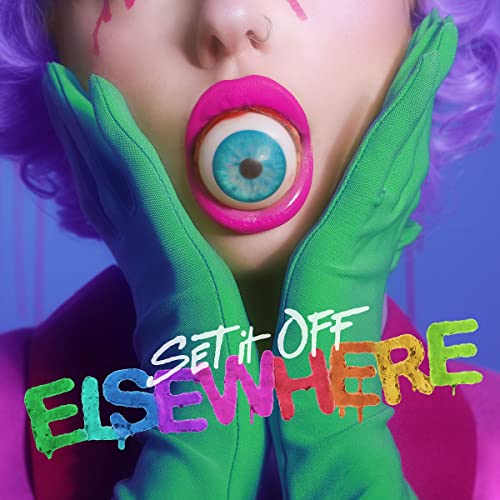 Person with purple hair and green gloves holding a large eyeball in their mouth.