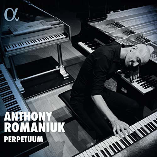 Anthony Romaniuk sits at a piano surrounded by multiple keyboard instruments in black and white.