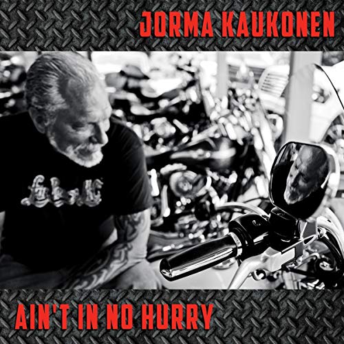 Jorma Kaukonen sits by a motorcycle with his reflection visible in the side mirror.