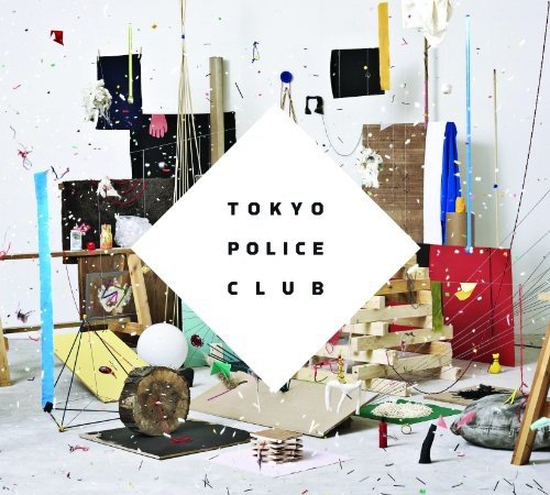 "Album cover with 'TOKYO POLICE CLUB' text on white diamond, amidst messy art studio."