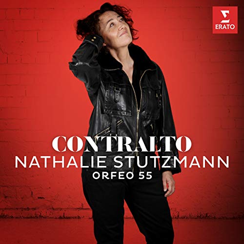 A woman in black leather stands against a red brick wall, album cover artwork.