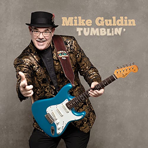Mike Gulden, a smiling musician with a guitar, wearing a hat and jacket.