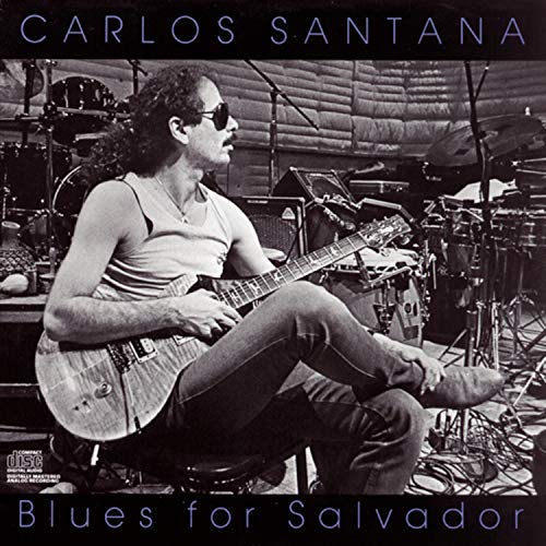 "Album cover with Carlos Santana playing guitar in a studio surrounded by drum kits."