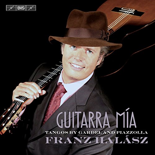 Man in suit and hat holding a guitar against a black background.