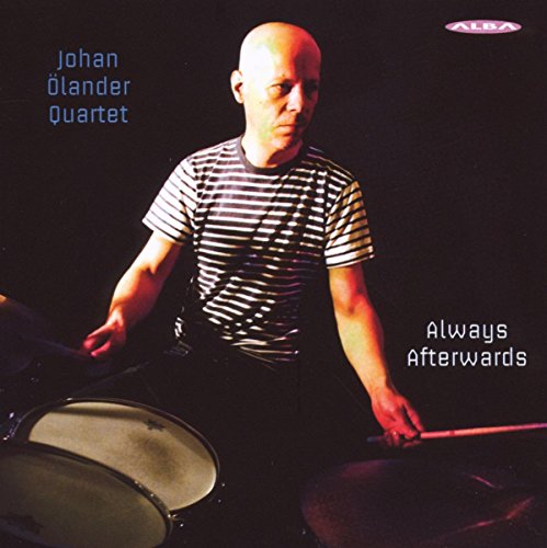 "CD cover featuring a bald man playing drums against a dark background."