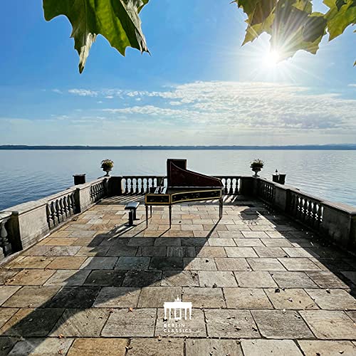 Piano on a stone terrace overlooking a lake under a bright sun.
