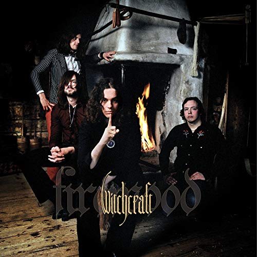 Four musicians with long hair pose before a stone fireplace and flames.