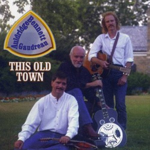 "Album cover featuring three men with guitars in a grassy outdoor setting."