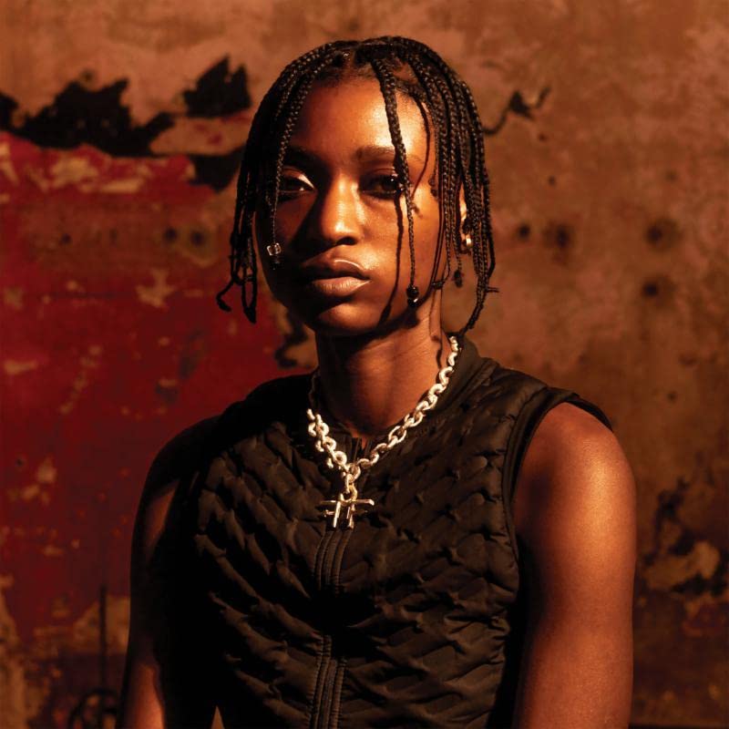 Close-up portrait of a young Black man with braided hair and jewelry.