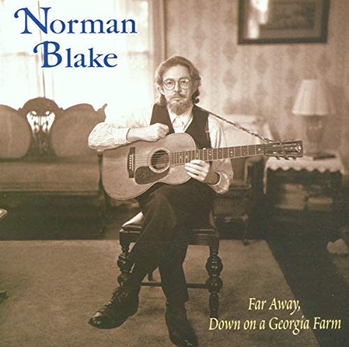 Norman Blake seated, playing acoustic guitar in a room.