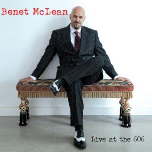 Benet McLean sits on a patterned bench, wearing a black pinstripe suit and red tie.