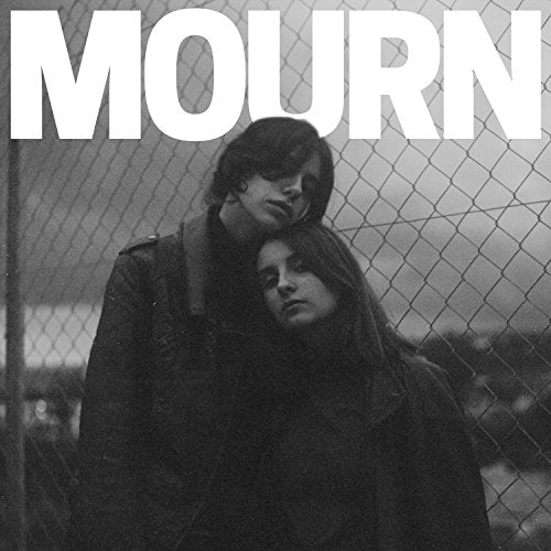 Black and white photo of two people leaning together in front of a chain-link fence.