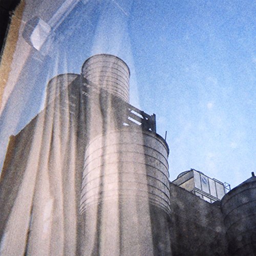 Grain silos against a bright, hazy blue sky, album cover art.