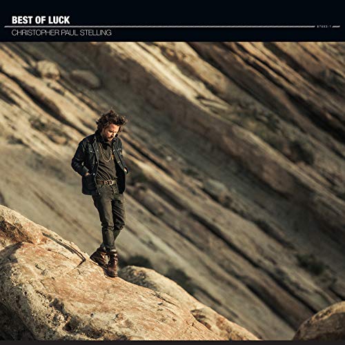 "Album cover with a man standing on a rocky outcrop, wearing dark clothing."