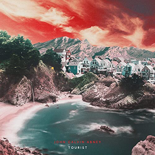 Coastal town with colorful buildings beneath mountains, album cover art.