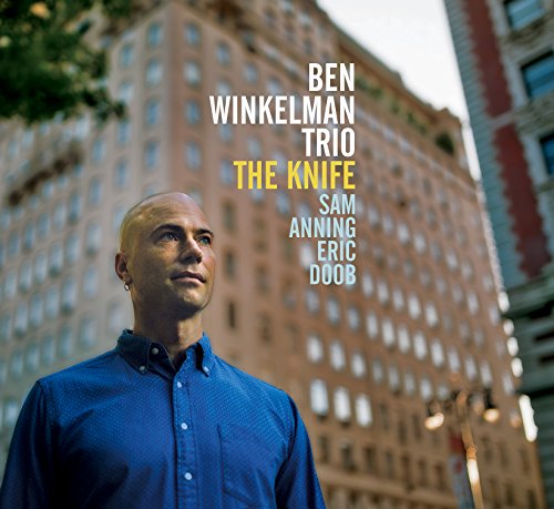 Album cover featuring a man in a blue shirt with cityscape background.