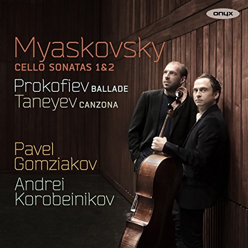 Two men in suits, one holding a cello, against a wood-paneled wall.
