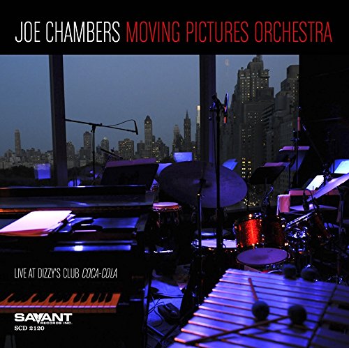"Album cover with a stage featuring musical instruments and a city skyline at dusk."