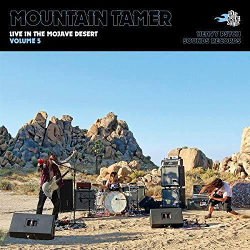 Band performing outdoors with rock formations and desert landscape backdrop.