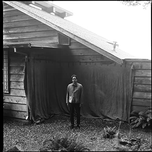 Black and white portrait of a man standing in front of a wooden building.