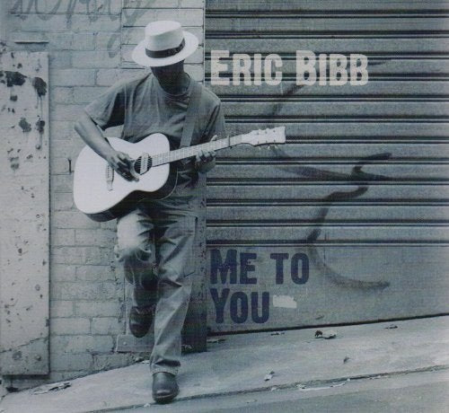 "Album cover featuring a man in a hat playing guitar by a graffiti-covered wall."