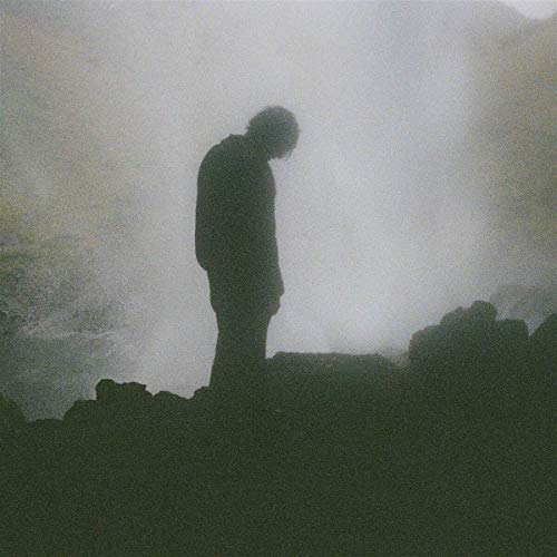 Silhouetted figure with head bowed, set against a hazy, dark background.