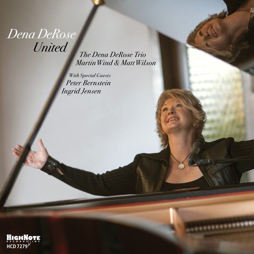 Jazz singer Dena DeRose with arms outstretched, standing behind a grand piano.