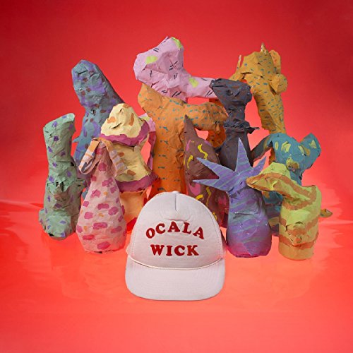 A white baseball cap with "Ocala Wick" in red, surrounded by colorful abstract paper sculptures.