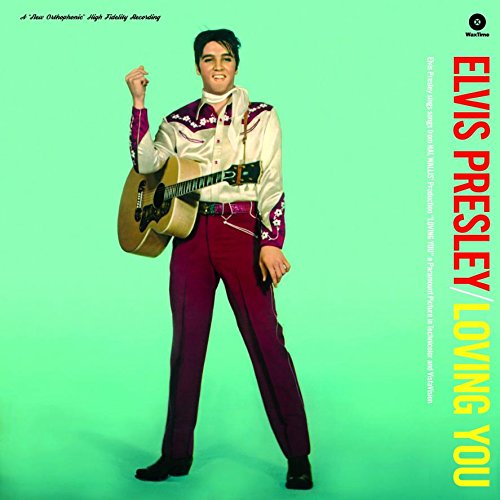 Elvis Presley standing against a green background, playing an acoustic guitar and wearing western-style clothing.