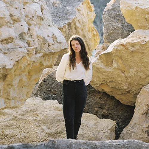 Woman with long brown hair standing amongst large rock formations.