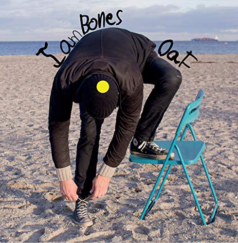 Person in black clothing tying shoelaces on a beach beside a blue folding chair.