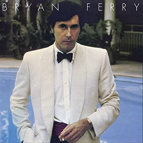 Bryan Ferry wearing a white tuxedo jacket and bow tie by a swimming pool.