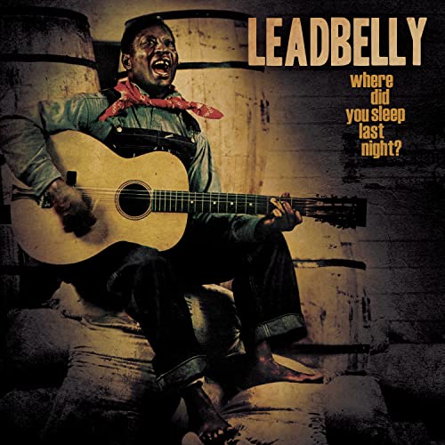 Leadbelly playing guitar, album cover with rustic barrel background.