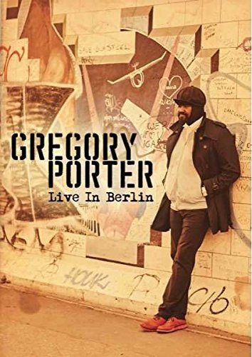"Man in dark jacket and hat standing by a graffiti-covered wall, 'Gregory Porter Live In Berlin'."