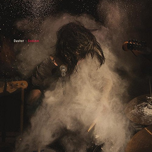 Musician performing with a microphone amidst a cloud of dust and instruments.