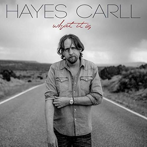 "Album cover featuring a man standing on a road with text 'Hayes Carll - what it is'."