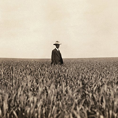 Sepia-toned photo of a man in a suit and hat in a field.