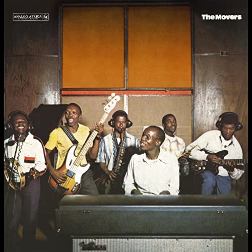 Six Black musicians with instruments posing in front of studio equipment.