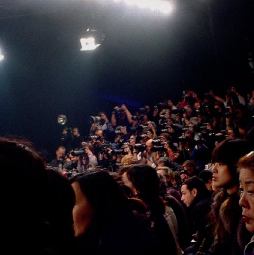 Crowd of people with cameras focused on a brightly lit stage.
