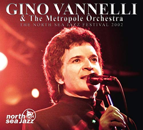 Gino Vannelli singing into a microphone on a concert stage.